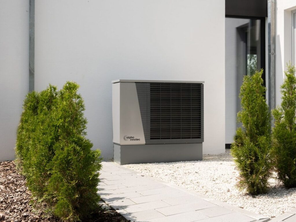 Unidad exterior de aerotermia instalada en la fachada de una vivienda unifamiliar de obra nueva, con jardín recién ajardinado